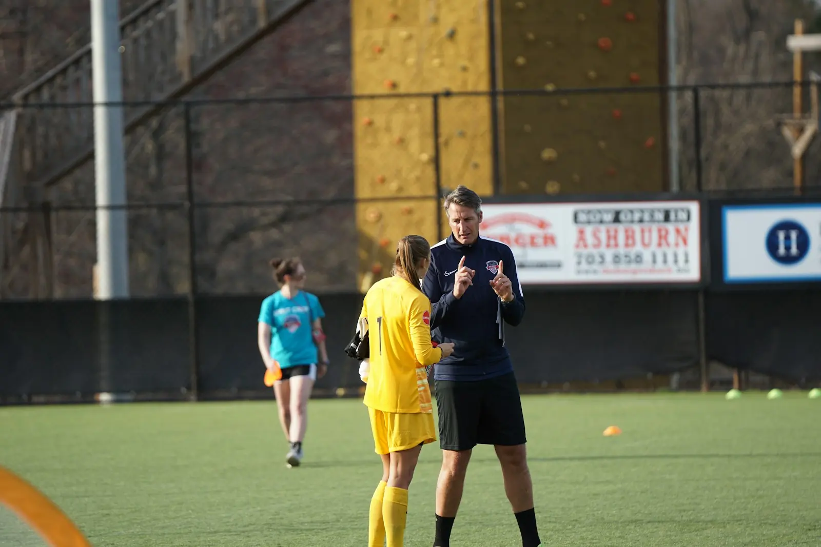 A goalkeeper in yellow listens to her coach at a women's soccer training session