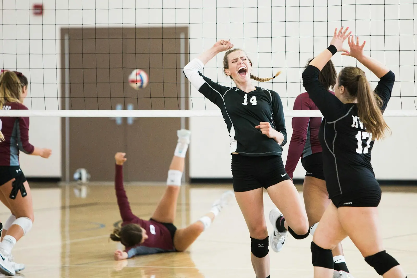 Women's volleyball players celebrate a point at the net during an indoor match