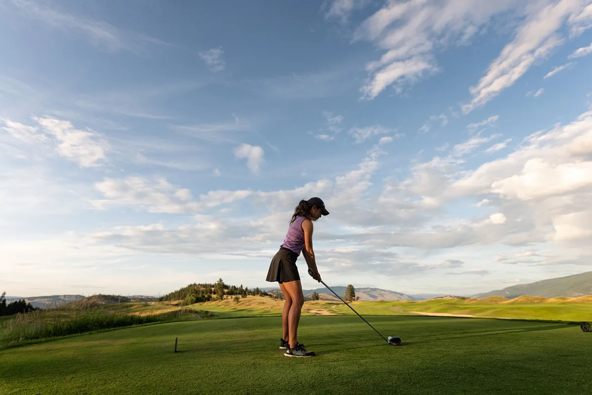 A woman golfer addresses the ball on a wide fairway beneath a big sky